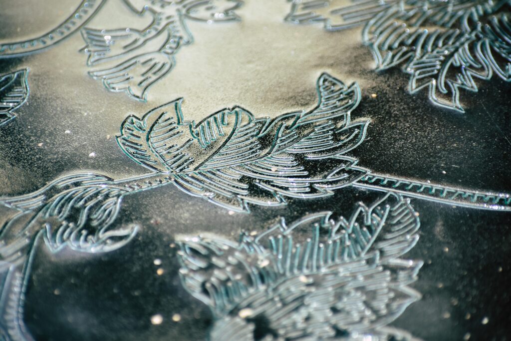 Close-up of detailed leaf patterns etched into frosted glass with a textured finish.
